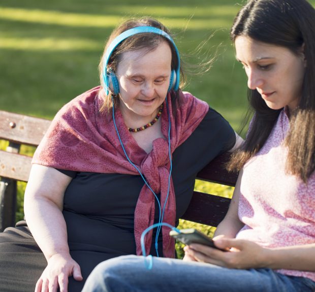 Woman with Down Syndrome and her friend having fun and listening music in a park.